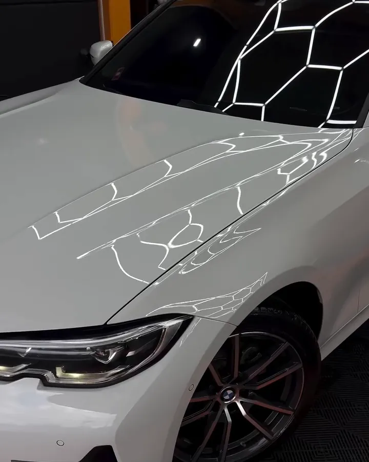 BMW branca com a pintura espelhando a iluminação hexagonal do box